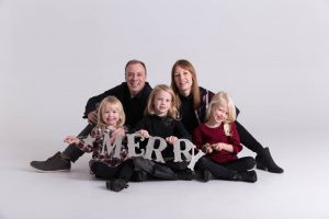 Family portrait for Christmas in the studio with a glitter sign that says MERRY